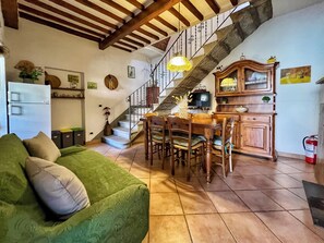 A cozy living room with a green sofa, wooden dining table, and chairs, a kitchen area with a wooden cabinet, and a staircase with a wrought iron railing. - Un Angolo nel Borgo - Two Bedroom Apartment, Sleeps 7 (Camucia)