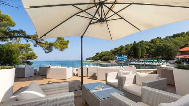 A seaside patio with wicker furniture, a large umbrella, and a view of the sea and a pool area. - Gorgeous apartment in Porec with WiFi (Porec)