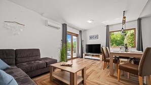 Un salon moderne comprenant un canapé, une table basse, un téléviseur et un coin repas avec des chaises et une table.