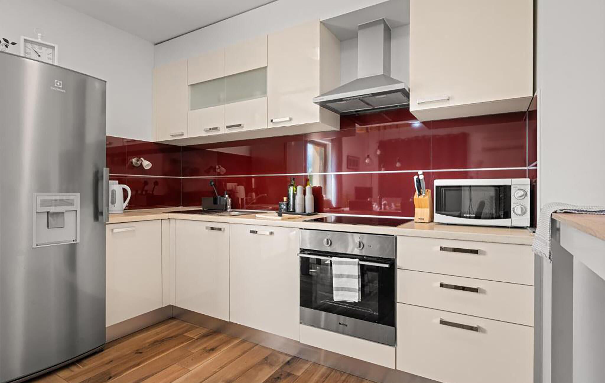 A modern kitchen with stainless steel appliances, white cabinetry, and a red backsplash.