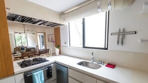 A modern kitchen with a gas stove, dishwasher, and a large window providing natural light. - Duplex en el Primer Parque de laureles (Medellín)