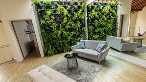 A modern living room with a grey sofa, a small round table, and a grey furry rug. A vertical garden with various plants is behind the sofa. - Duplex en el Primer Parque de laureles (Medellín)
