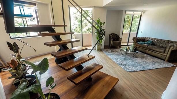 A modern living room with a wooden staircase, a sofa, and potted plants. - Duplex en el Primer Parque de laureles (Medellín)