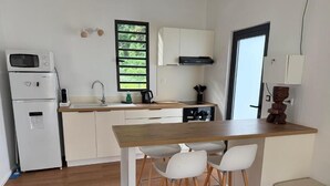 Een compacte keuken met witte kastjes, een houten aanrechtblad en een ingebouwde kookplaat. Er staan twee witte stoelen bij het aanrecht en een klein krukje.