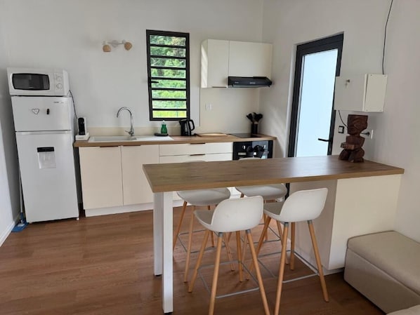 Una cocina compacta con armarios blancos, una encimera de madera y una estufa empotrada. Hay dos sillas blancas en la encimera y un taburete pequeño.