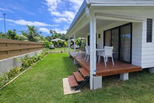 A modern house with a covered porch, a grassy backyard, and a wooden deck.