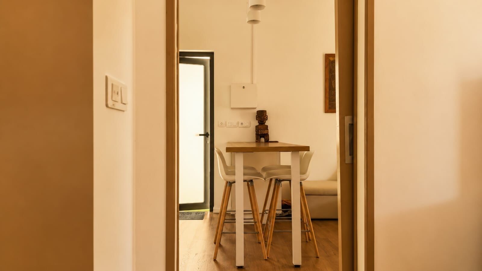 Un pasillo que conduce a un comedor con una mesa y sillas, una lámpara y una puerta.
