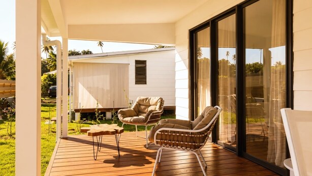 A covered outdoor area with a wooden deck, two wicker chairs, and a small table.