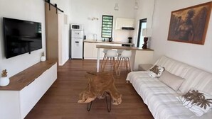 A modern living room with a flat-screen TV, a sofa, and a dining area with a table and chairs.