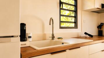 Una cocina con un lavamanos doble, una ventana con persianas, una cafetera y un recipiente con la etiqueta 'KRUPS'.