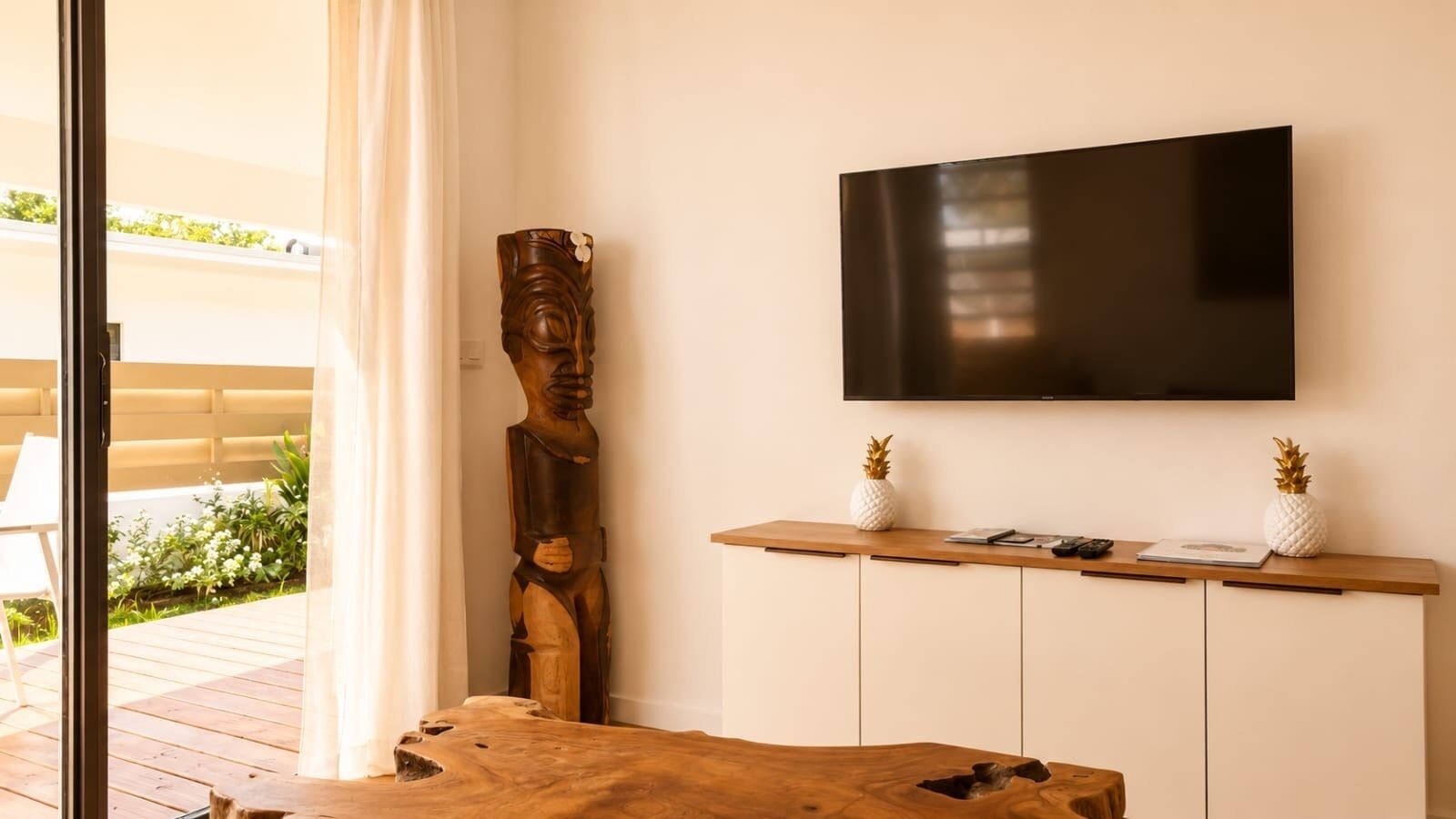 Una sala de estar moderna con una mesa de centro de madera, un televisor de pantalla plana grande montado en la pared y una escultura decorativa de madera.