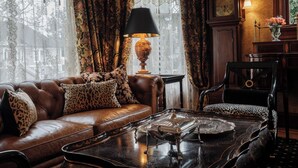 Una sala de estar acogedora con un sofá de cuero, cojines estampados, una mesa de centro con una bandeja, una lámpara y un reloj en la pared.