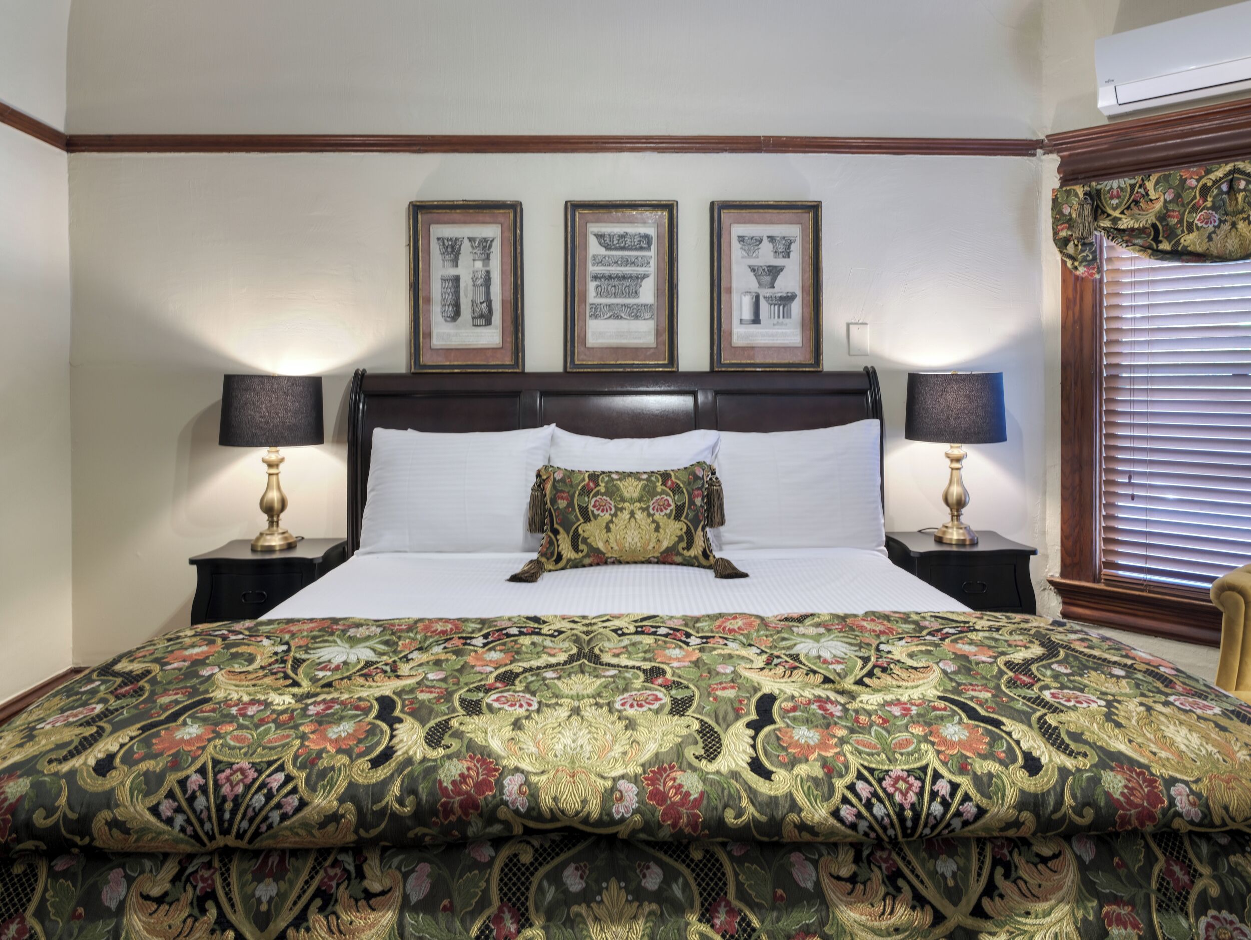 Un lit bien fait, recouvert d’une couvre-lit à motifs floraux, avec deux lampes de chevet et trois tableaux encadrés accrochés au-dessus de la tête de lit.