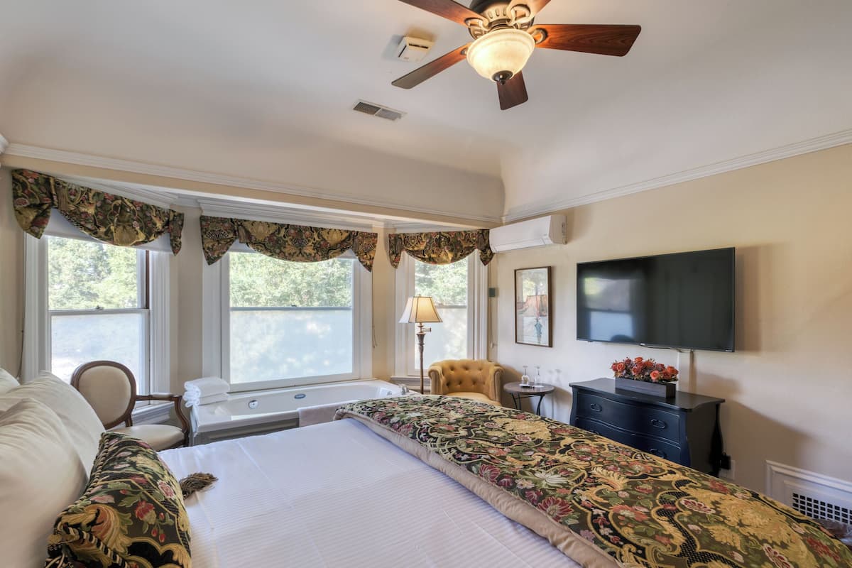 Une chambre d’hôtel avec un grand lit, un ventilateur de plafond, un téléviseur à écran plat, un bureau et une chaise.