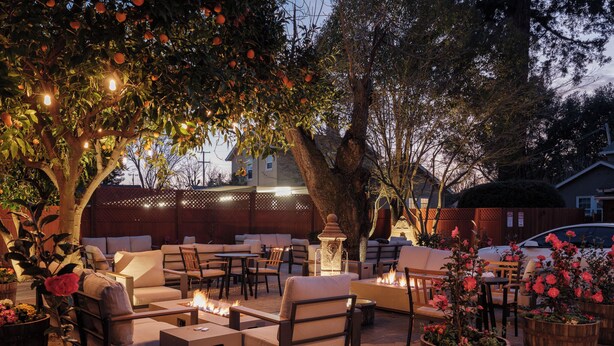 Un patio al aire libre con arreglos de asientos, un hogar para fuego y luces decorativas.