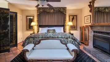 A hotel room with a large bed, a fireplace, a ceiling fan, and a large mirror.