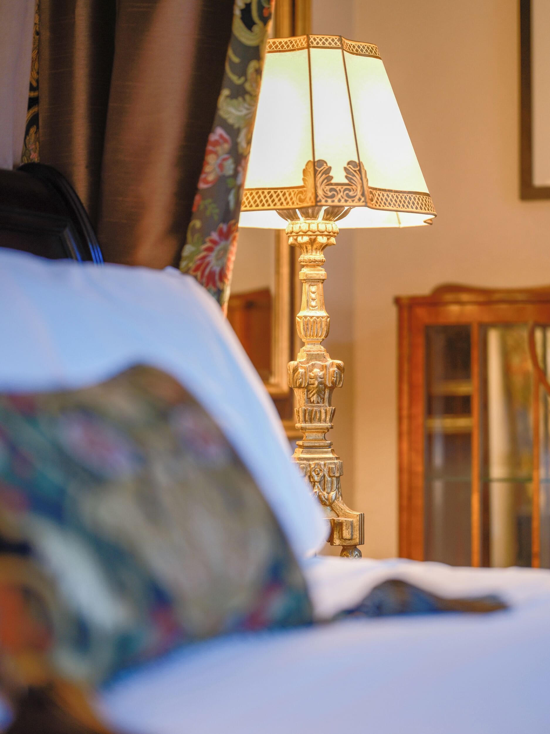 Una cama con un almohadón floral y una lámpara decorativa con pantalla estampada.