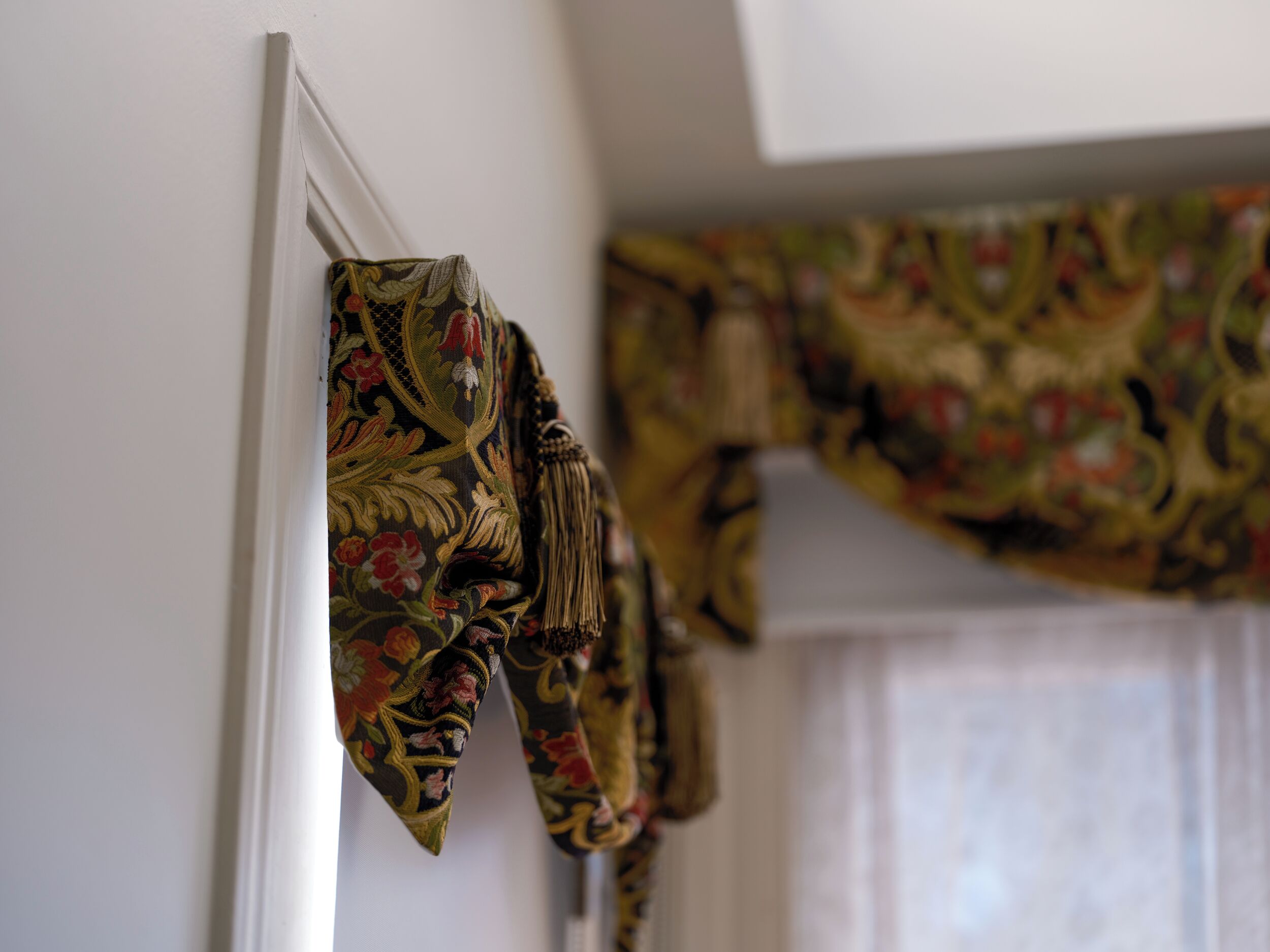 A window with a floral curtain and a matching tie hanging on the wall.