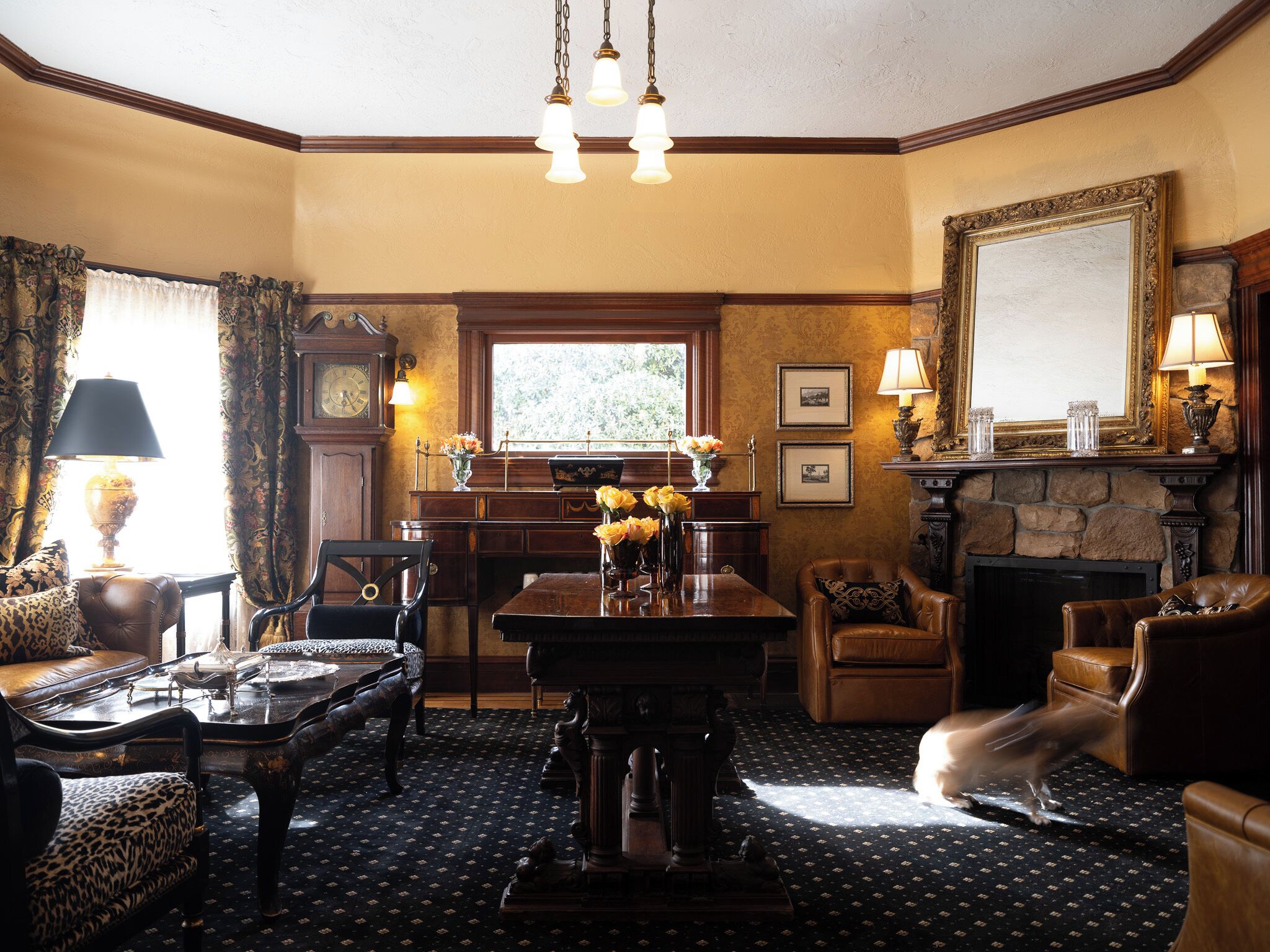 A traditional room with a wooden desk, leather chairs, a fireplace, and a large mirror.