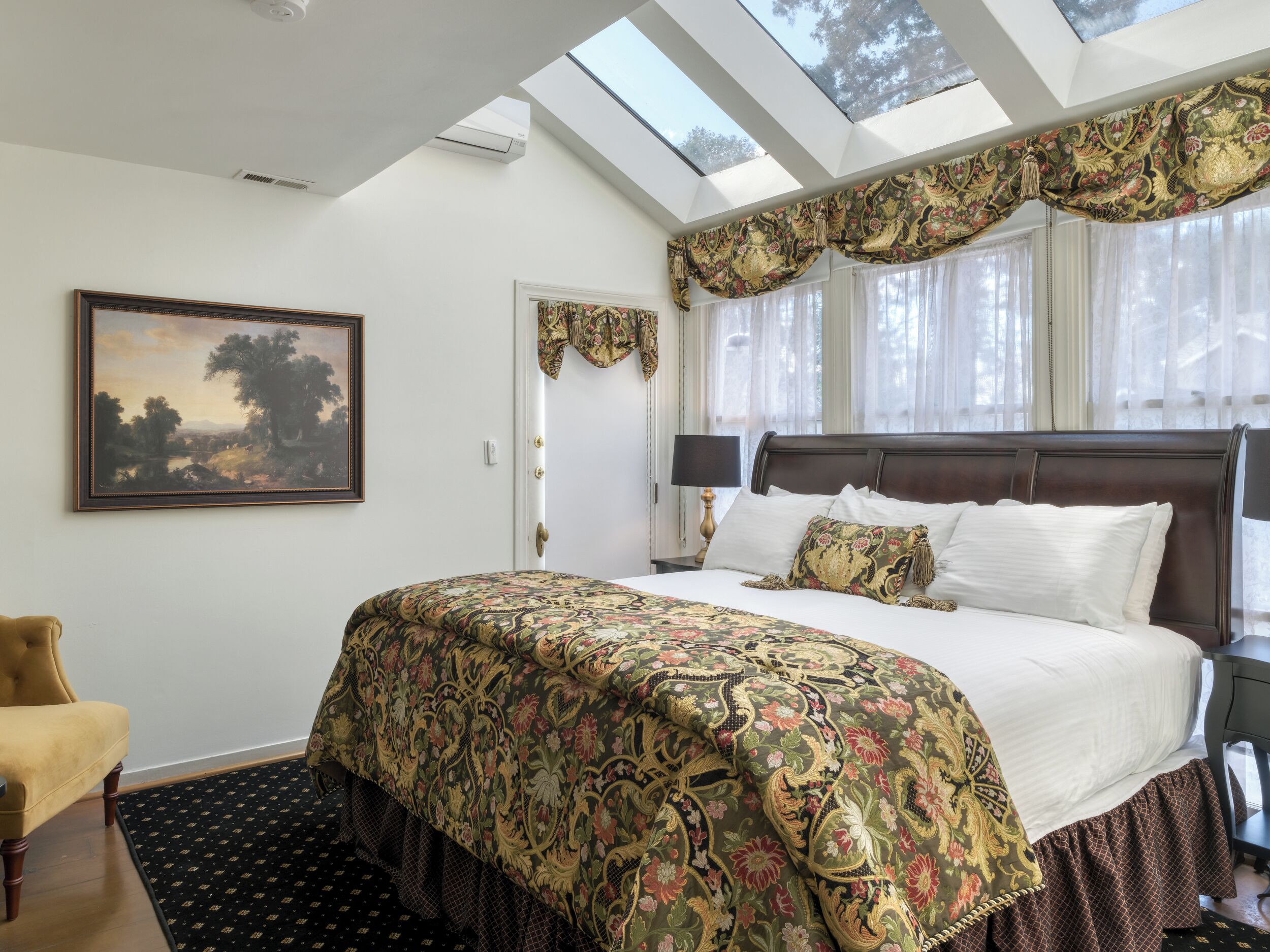 Ein Schlafzimmer mit einem großen Bett, einem Bild an der Wand, einem Fenster mit Vorhängen und einem Dachfenster.