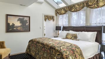 A bedroom with a large bed, a painting on the wall, a window with curtains, and a skylight.