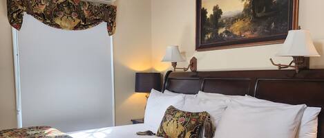 A neatly made bed with a floral bedspread, two bedside lamps, and a framed landscape painting on the wall.