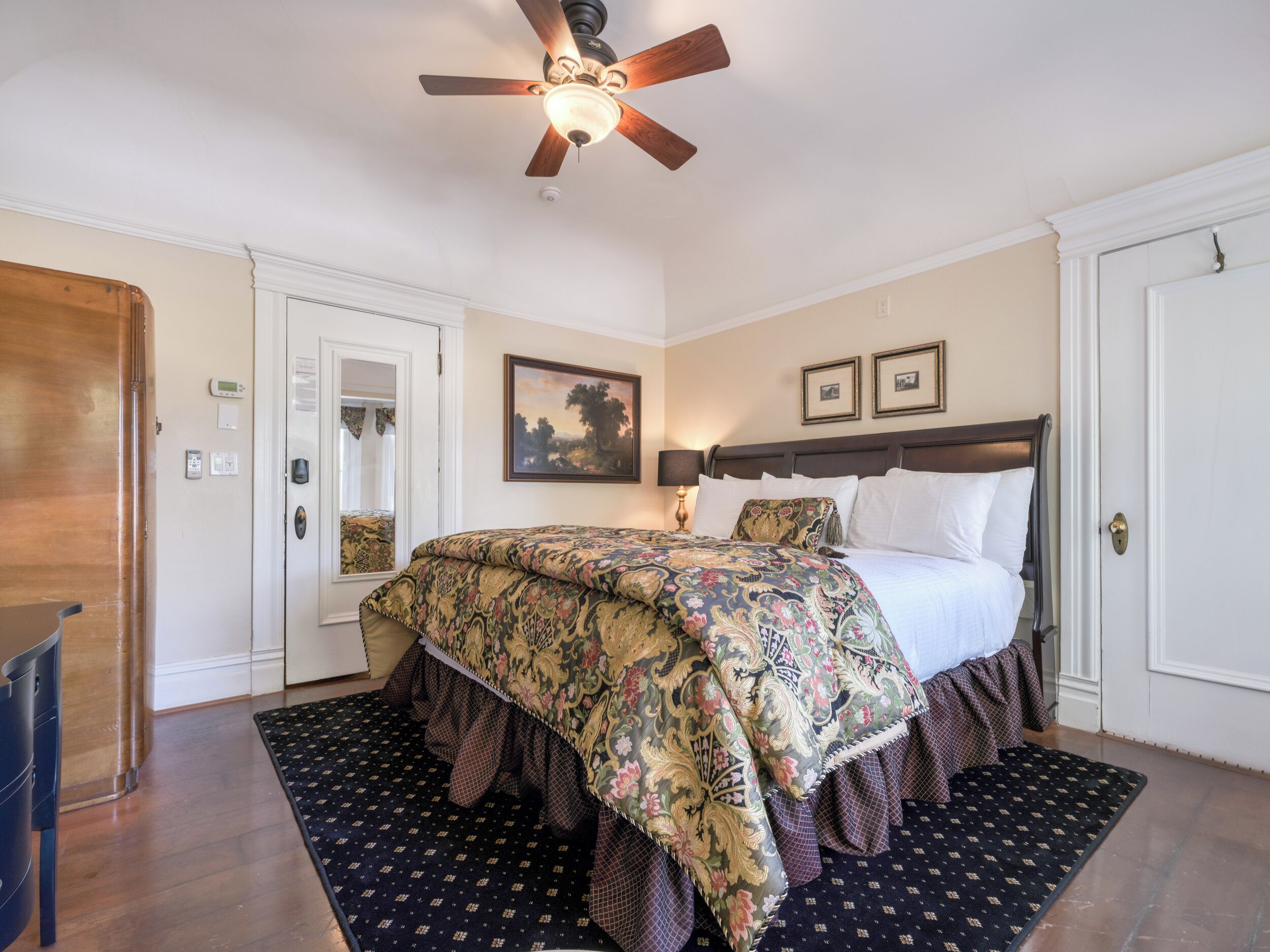 Une chambre à coucher avec un lit en bois, un ventilateur de plafond, une table de chevet avec une lampe et un tapis à motifs.