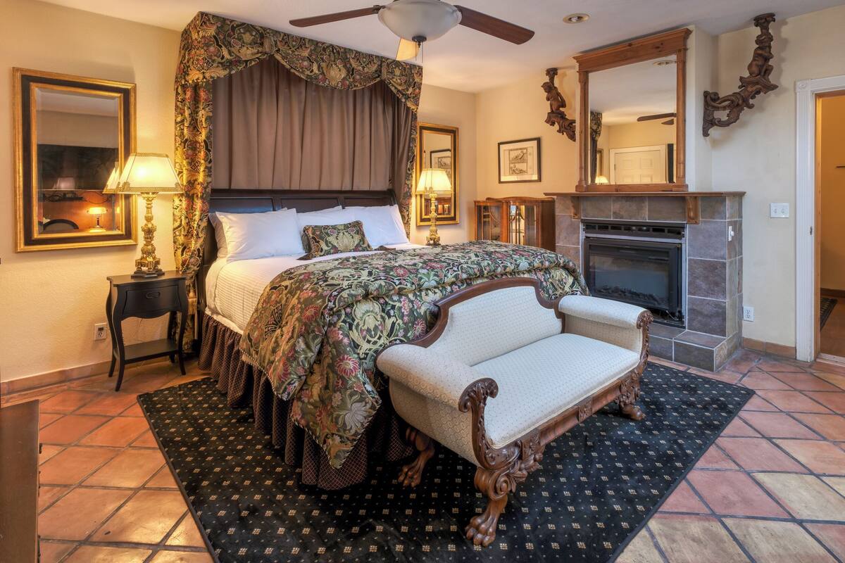 Une chambre à coucher de style traditionnel, dotée d’un lit à baldaquin, d’une cheminée et d’un ventilateur de plafond.
