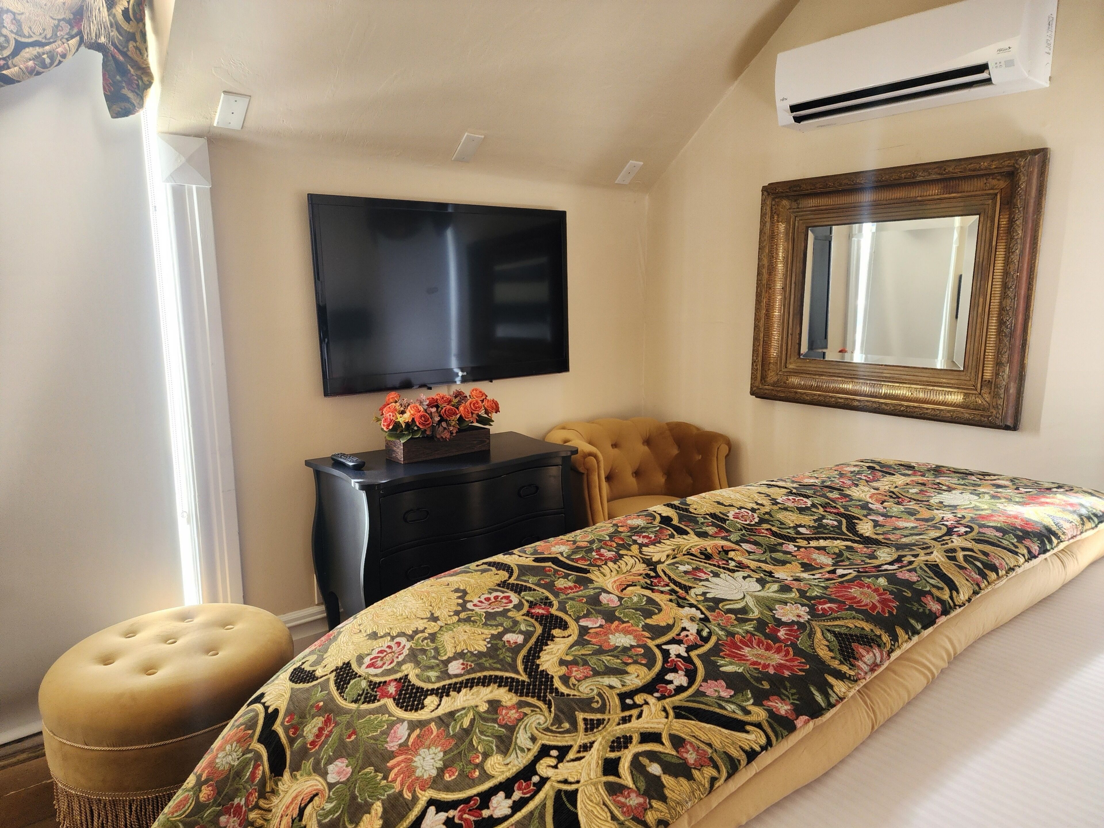 A hotel room with a bed, a television, a dresser, a mirror, and a window.