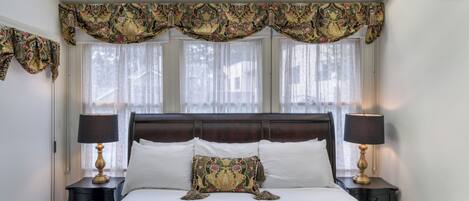 A bedroom with a large bed, two bedside tables with lamps, a decorative headboard, and a skylight above.