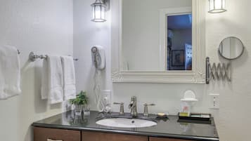 A bathroom with a large mirror, two wall-mounted lights, a towel rack, a hairdryer, and a sink with a dark countertop.