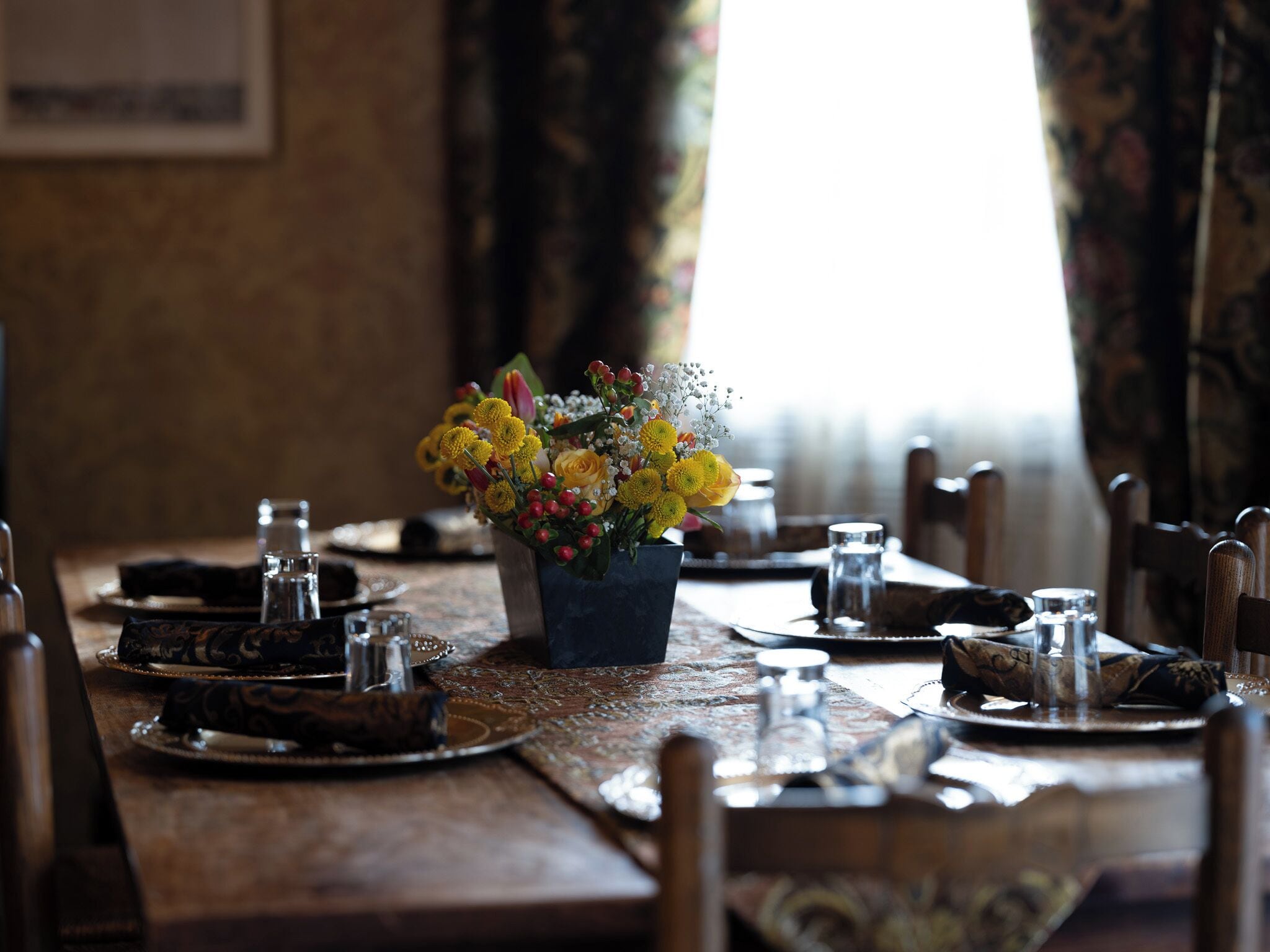 A dining table set with plates, glasses, and a vase of yellow flowers.