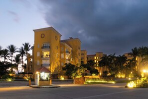 Et hotel med flere etager, altaner, en velbelyst indgang og et anlagt område med palmer.