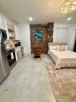 A compact room with a kitchenette, a bed, a seating area, and a brick accent wall. - Park Hotel Studio Suite 207 (Chattanooga)