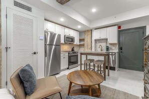 Une cuisine moderne avec des meubles blancs, des appareils en acier inoxydable et une table à manger en bois, accompagnée de deux tabourets.