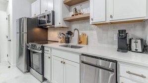 Una cocina moderna con electrodomésticos de acero inoxidable, armarios blancos y una cafetera.