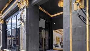 Fachada de edificio negra con adornos dorados y puerta de cristal que da al interior.