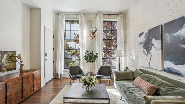 Un salon comprenant un canapé, une table basse et des fauteuils, une cheminée et une grande fenêtre avec des rideaux.