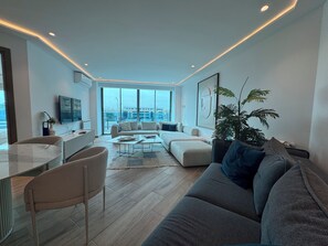 Uma sala de estar moderna com um sofá, mesa de centro e cadeiras. Há uma janela grande com vista para a cidade.