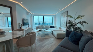Una sala de estar moderna con un sofá, una mesa de centro y sillas. Hay un ventanal con vistas a la ciudad.