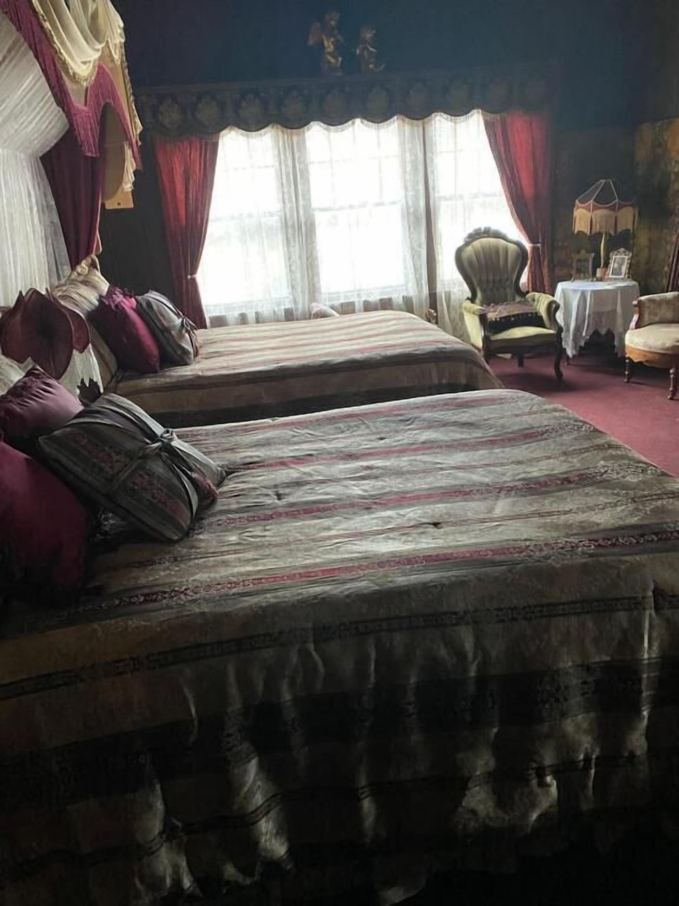 Une chambre avec deux lits, une chaise, une table et des rideaux.