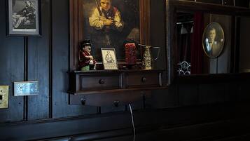 A room with a dark wooden wall, a framed portrait, a shelf with various items, and two wall-mounted lamps.
