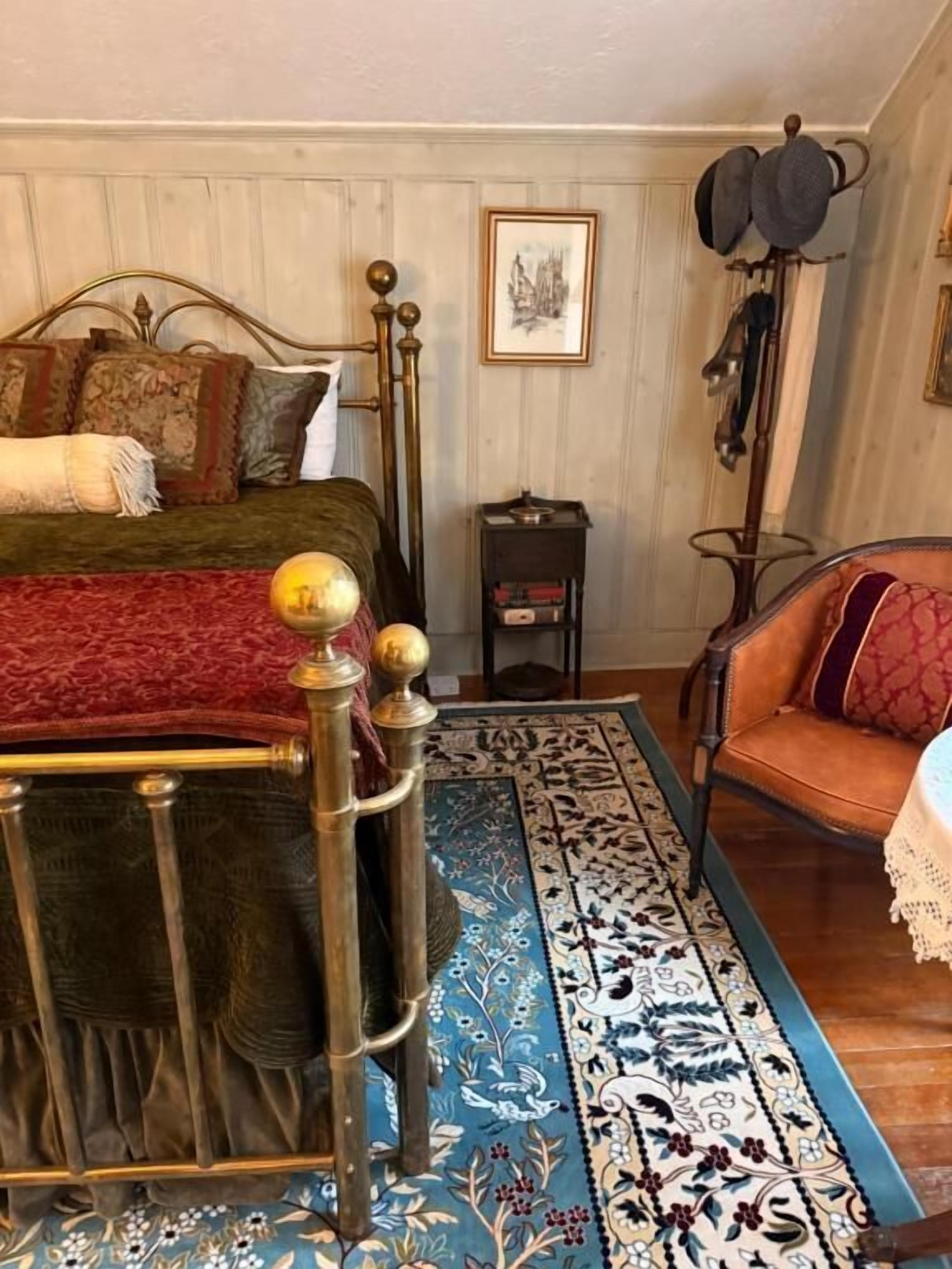 A traditional room with a four-poster bed, a patterned rug, a wooden chair, and a wall-mounted hat rack.