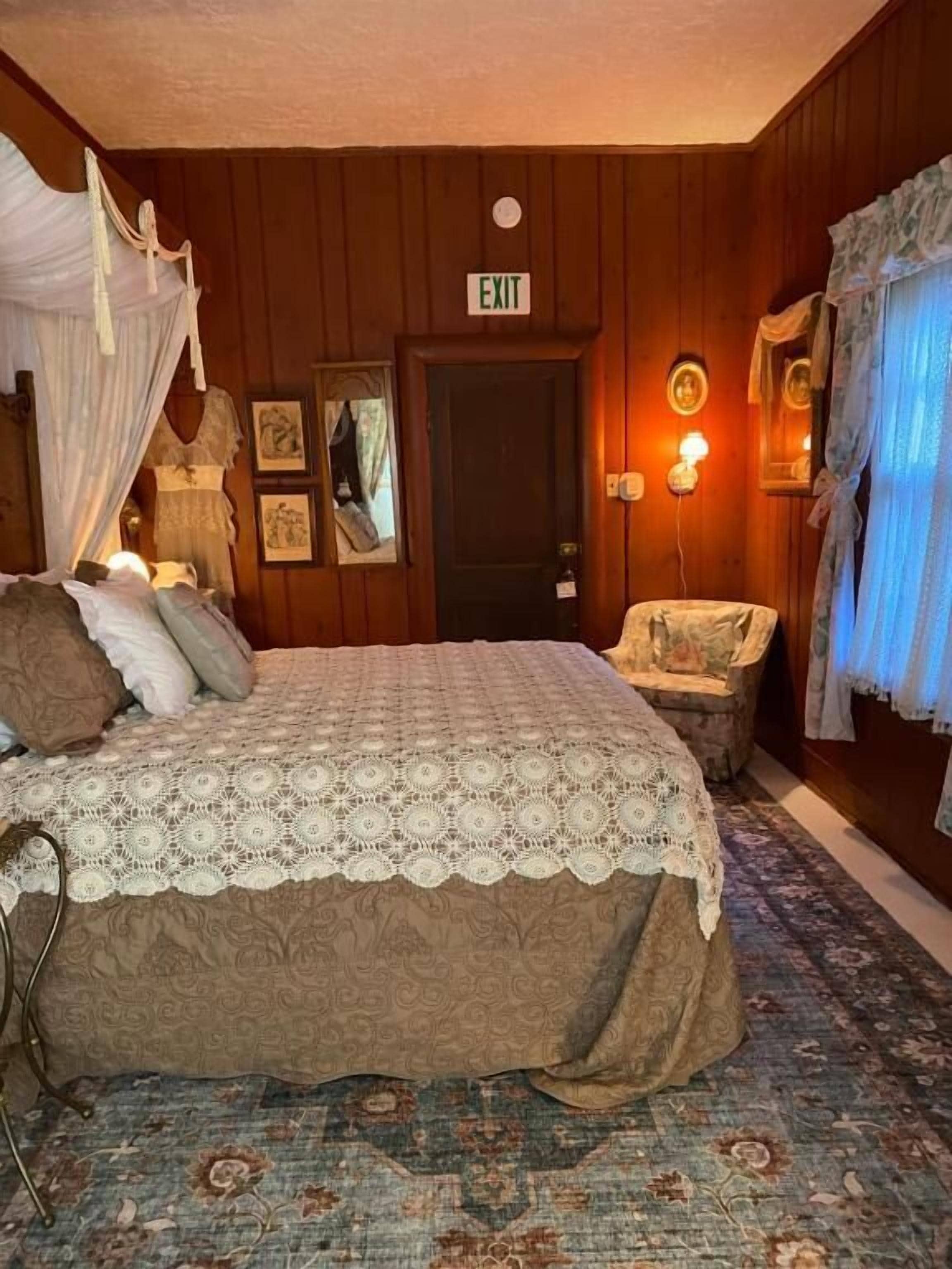 A bedroom with a bed, a chair, a door marked 'EXIT', and a wall-mounted lamp.