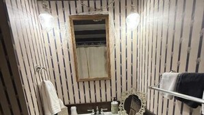 Un baño con lavamanos blanco, espejo y papel tapiz a rayas.
