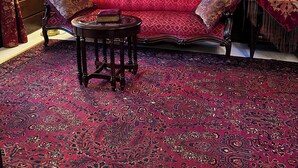Una habitación tradicional con un sofá rojo, muebles de madera ornamentados, una alfombra estampada y un globo en la pared.