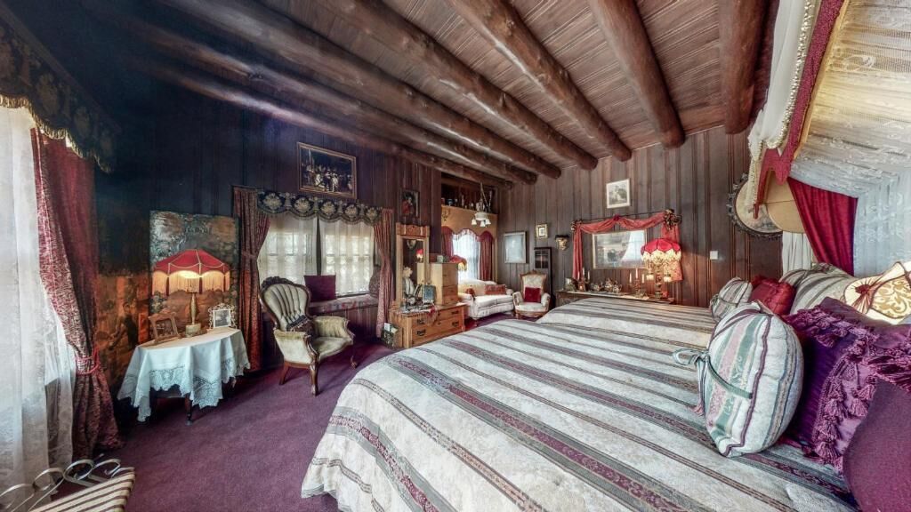Une pièce confortable avec un grand lit, des poutres apparentes en bois au plafond, une petite table avec une lampe et une chaise.