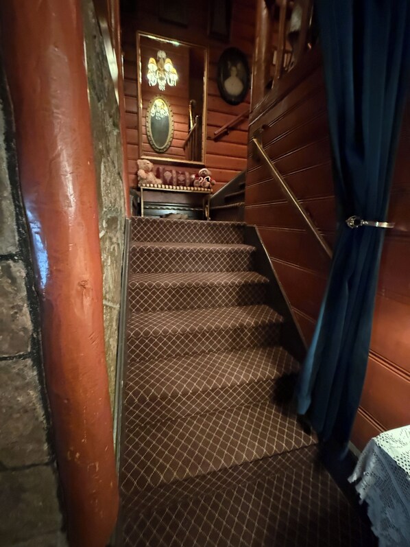 Un escalier recouvert d’un tapis à carreaux, un mur en bois, un lustre et un ours en peluche posé sur une étagère.
