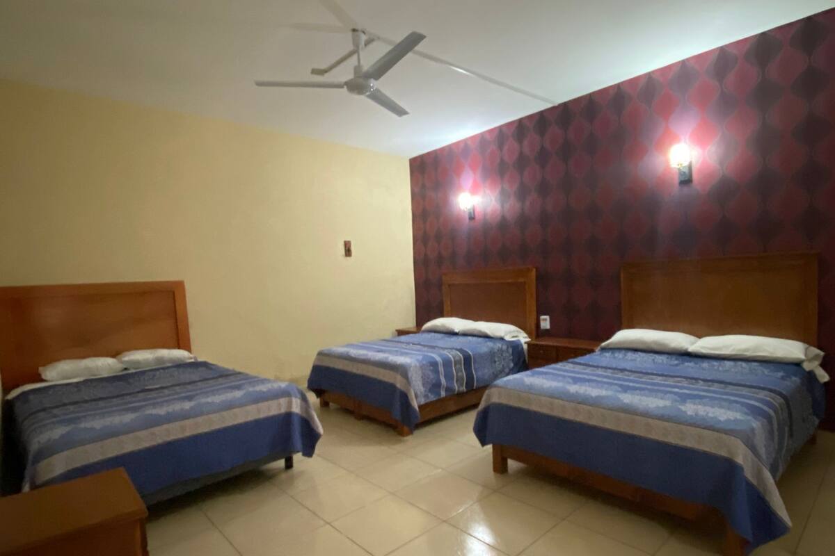 A hotel room with three single beds, a ceiling fan, and a patterned wall.