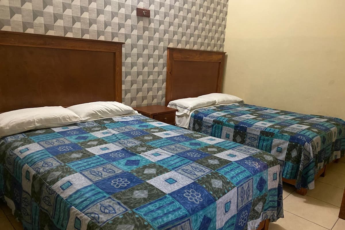 A room with two beds, each with a blue and green quilt, wooden headboards, and a geometric patterned wall.